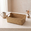The Market Basket, a woven straw basket with cut-out handles on a counter beside a pitcher and dried flowers