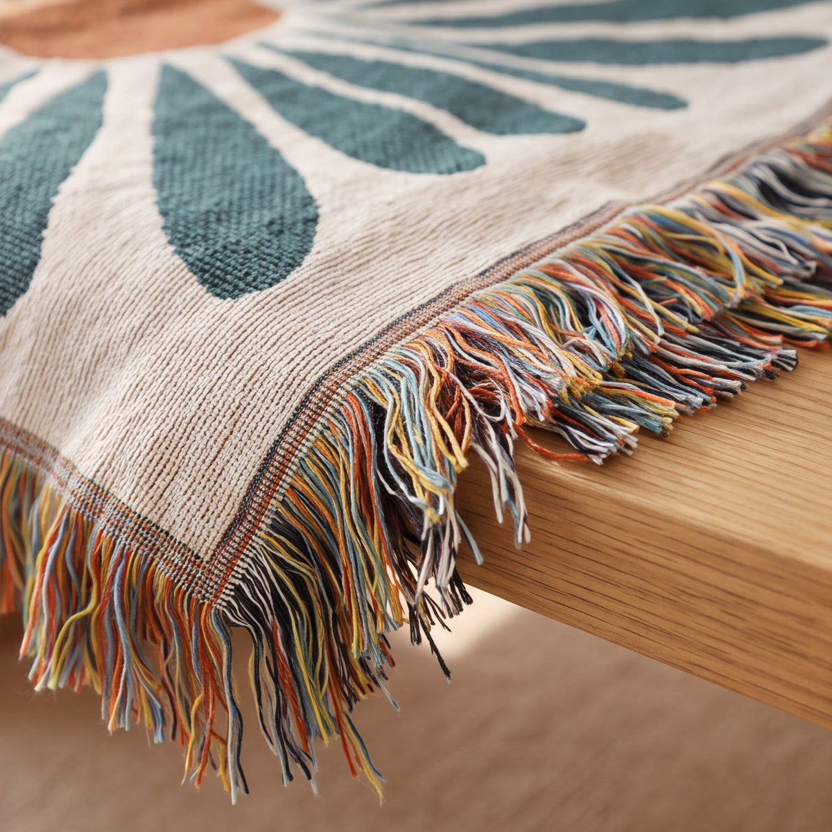 Fringed edge of the daisy print throw hanging over a wooden table