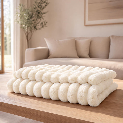 The Burrow Throw in Cream, an oversized ribbed faux fur blanket folded on a light oak table in a bright living room