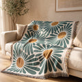 The Bloom Throw, a cream throw with an oversized green daisy print and rust centers, draped over a cream sofa