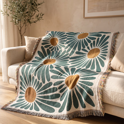 The Bloom Throw, a cream throw with an oversized green daisy print and rust centers, draped over a cream sofa