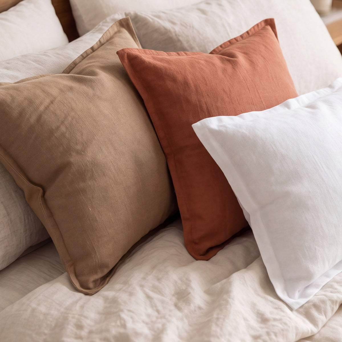 Close-up of Coffee, Terracotta and White linen-cotton pillow covers layered on a bed