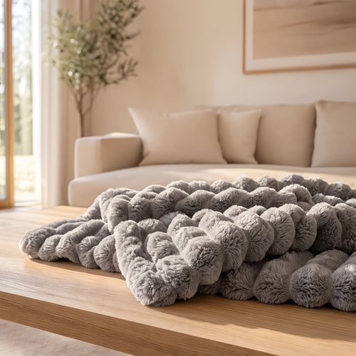 The Burrow Throw in Stone, a medium warm gray ribbed faux fur blanket folded on a wood coffee table